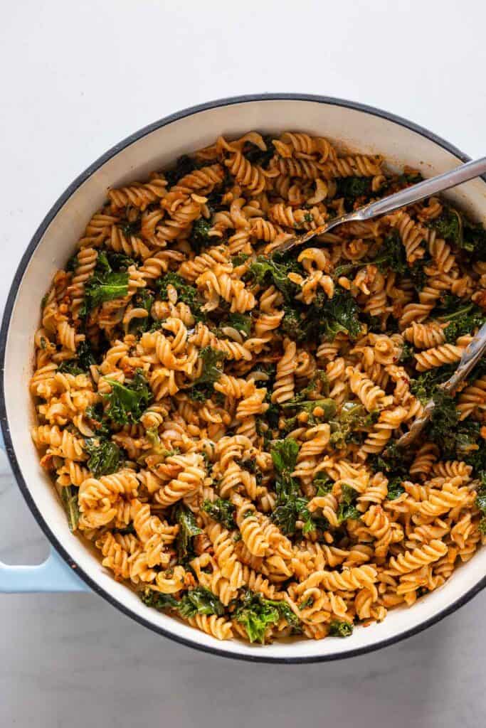 red pesto pasta in a large cooking pan with tongs