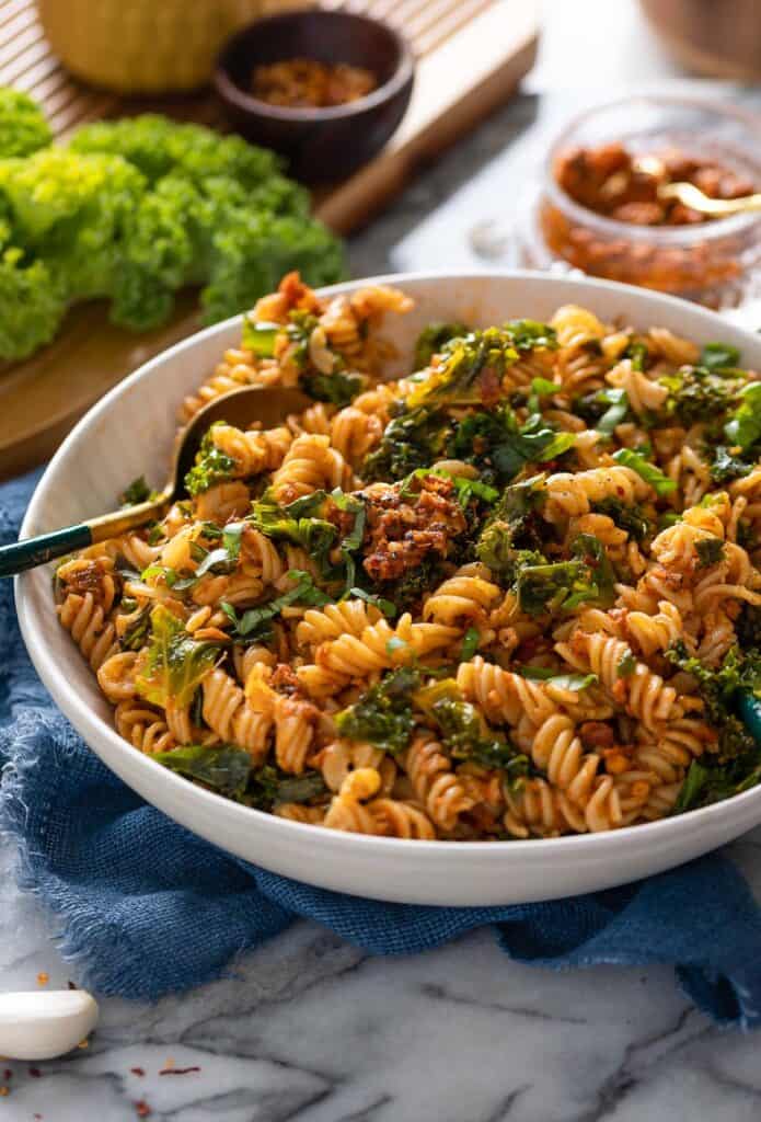 red pesto pasta with kale in a bowl with a serving spoon
