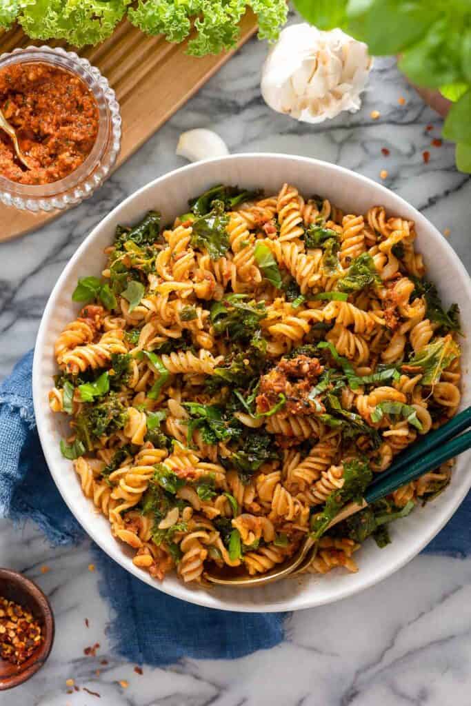 red pesto pasta in a serving bowl with pesto on the side
