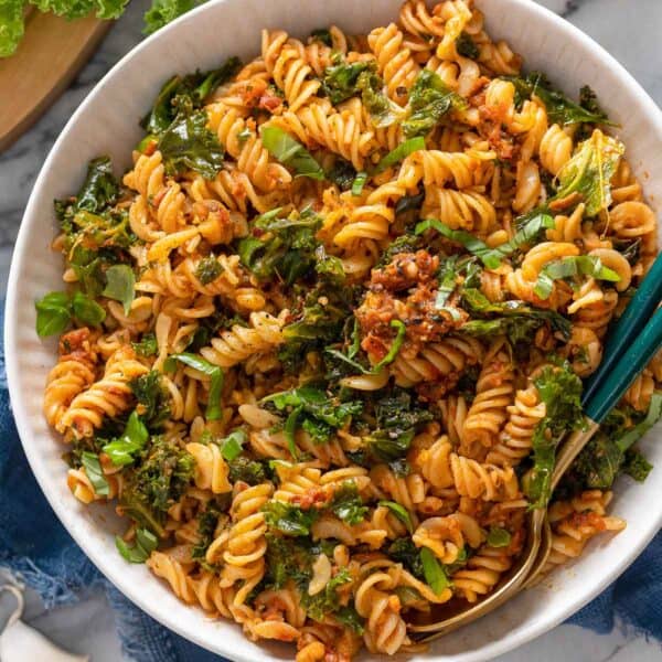 red pesto pasta topped with fresh basil and chili flakes in a serving bowl