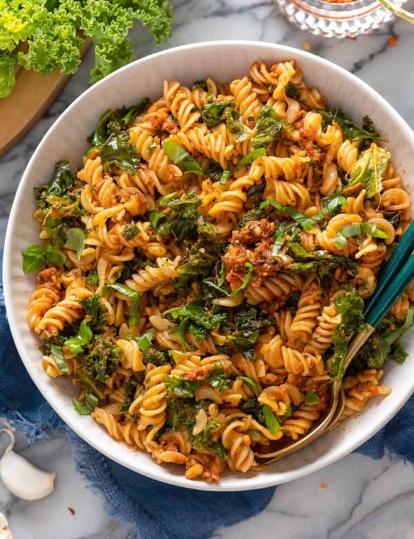 red pesto pasta topped with fresh basil and chili flakes in a serving bowl