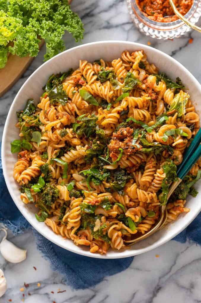 red pesto pasta topped with fresh basil and chili flakes in a serving bowl