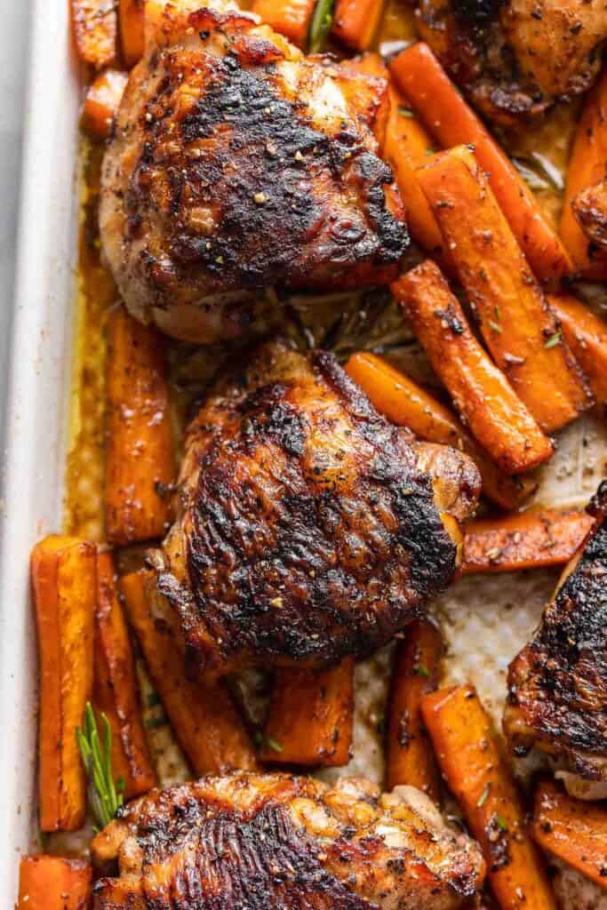 chicken thighs and carrot sticks covered in a balsamic glaze with rosemary on a baking tray