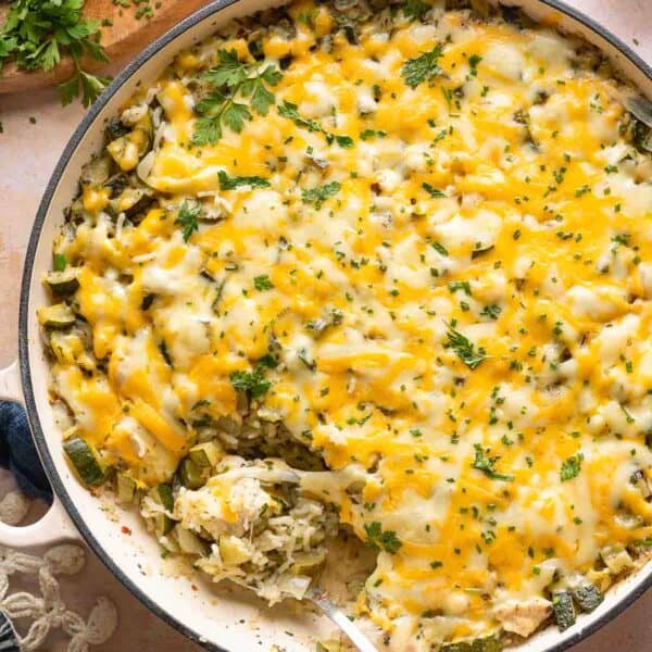 cheesy zucchini chicken and rice in a casserole dish with a serving spoon