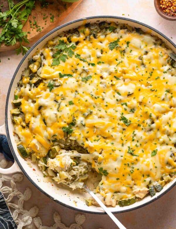 cheesy zucchini chicken and rice in a casserole dish with a serving spoon