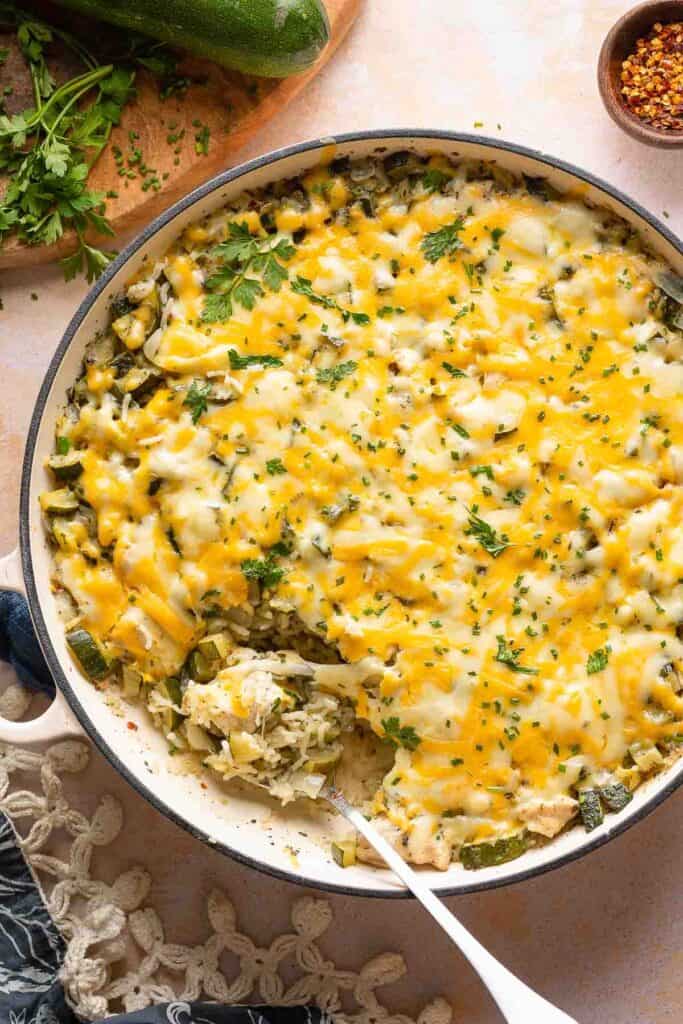 cheesy zucchini chicken and rice in a casserole dish with a serving spoon