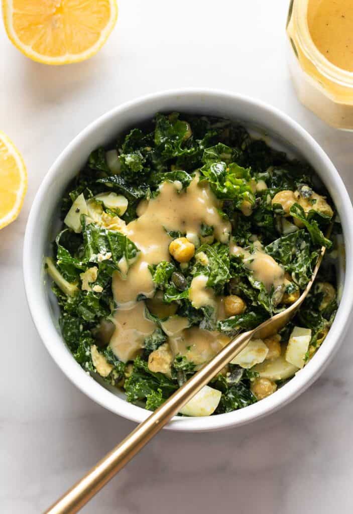 a kale salad in a bowl with chickpeas topped with a creamy lemon dressing