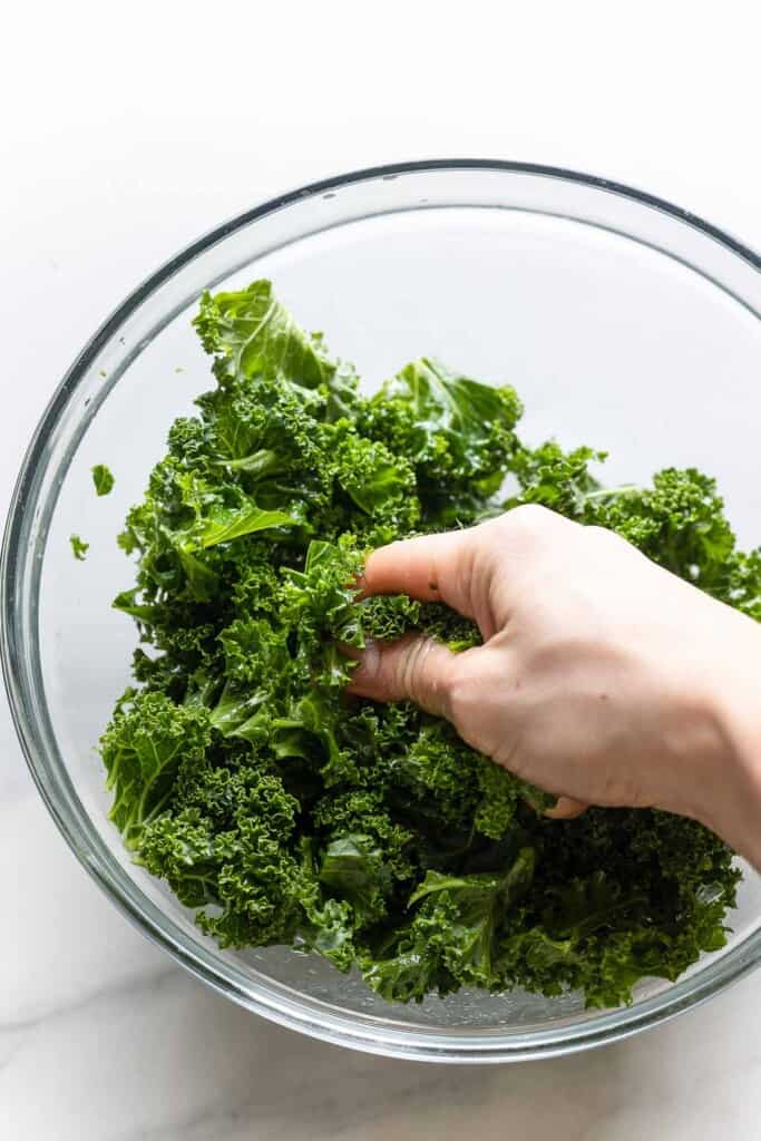 kale in a bowl getting rubbed with olive oil to soften the leaves