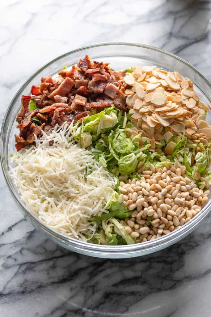 shredded brussels sprouts, chopped bacon, toasted almond flakes, pine nuts and parmesan cheese in a salad bowl