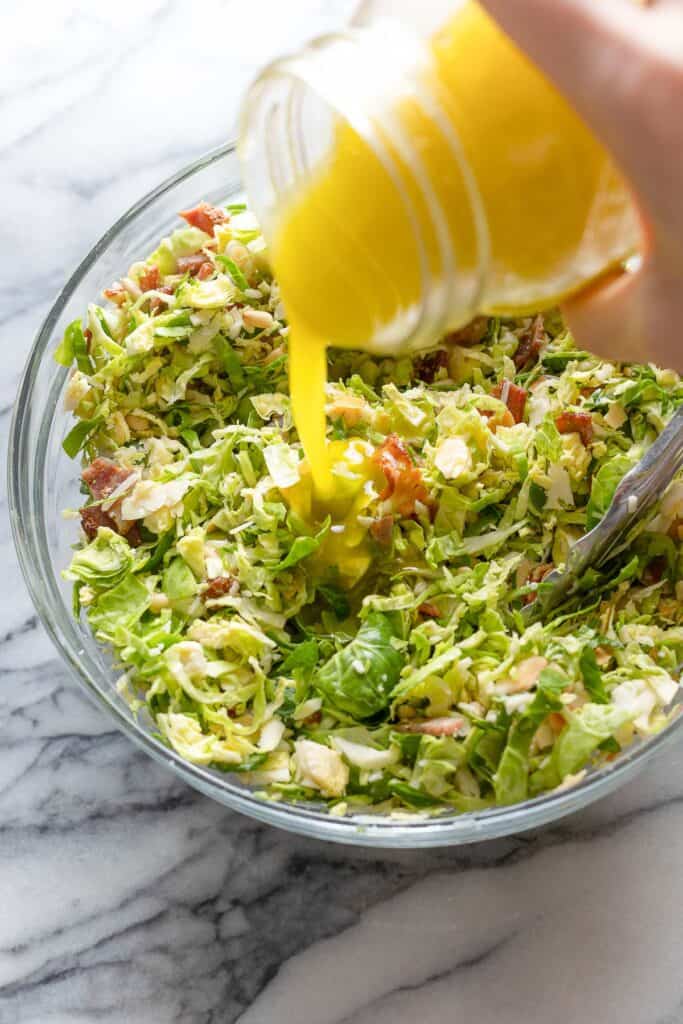 vinaigrette pouring into a shaved brussels sprout salad