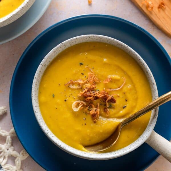 roasted acorn squash soup in a bowl with a spoon and topped with fresh thyme leaves and fried shallots