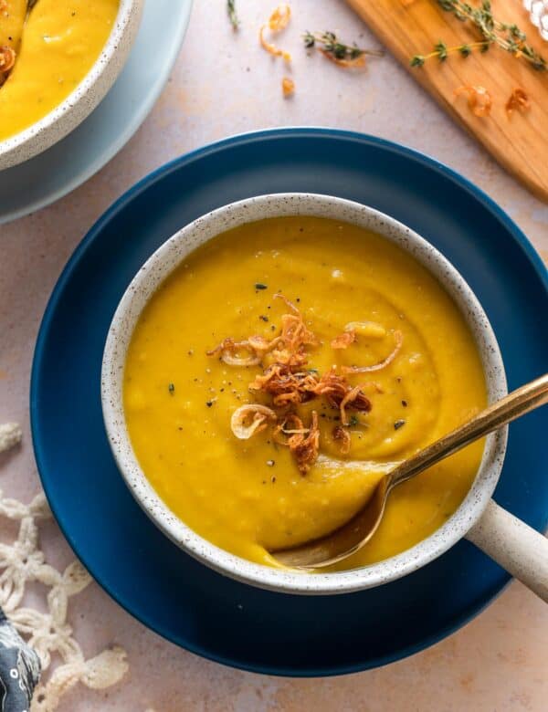 roasted acorn squash soup in a bowl with a spoon and topped with fresh thyme leaves and fried shallots