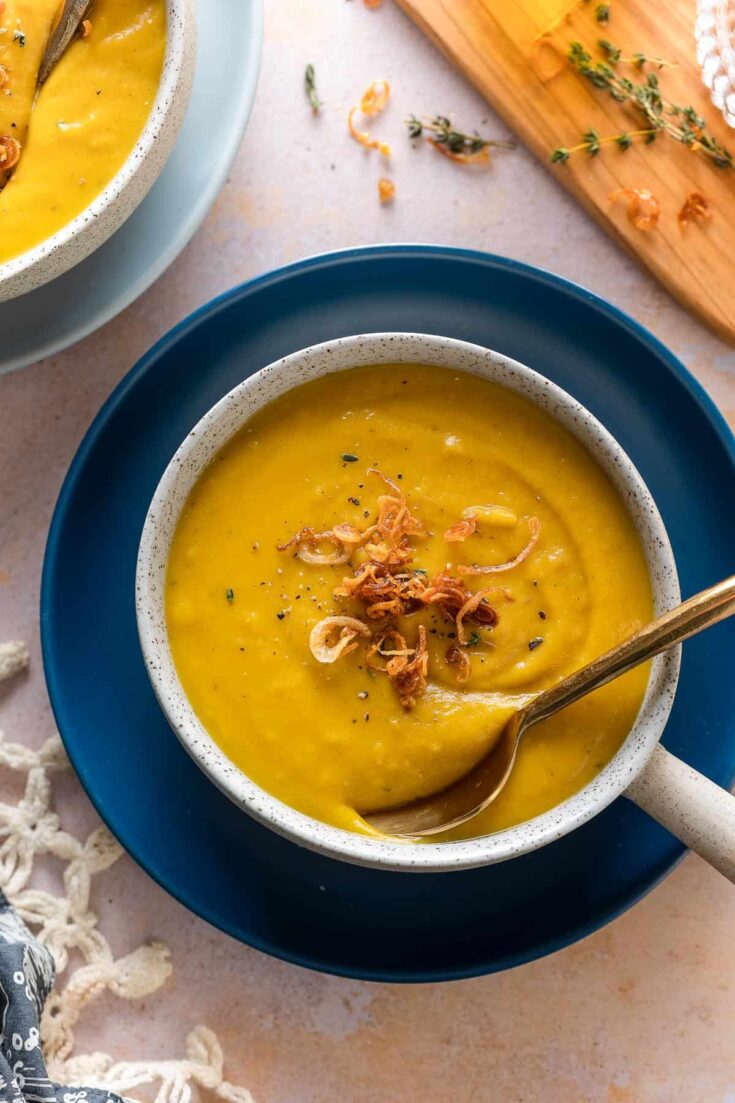 roasted acorn squash soup in a bowl with a spoon and topped with fresh thyme leaves and fried shallots