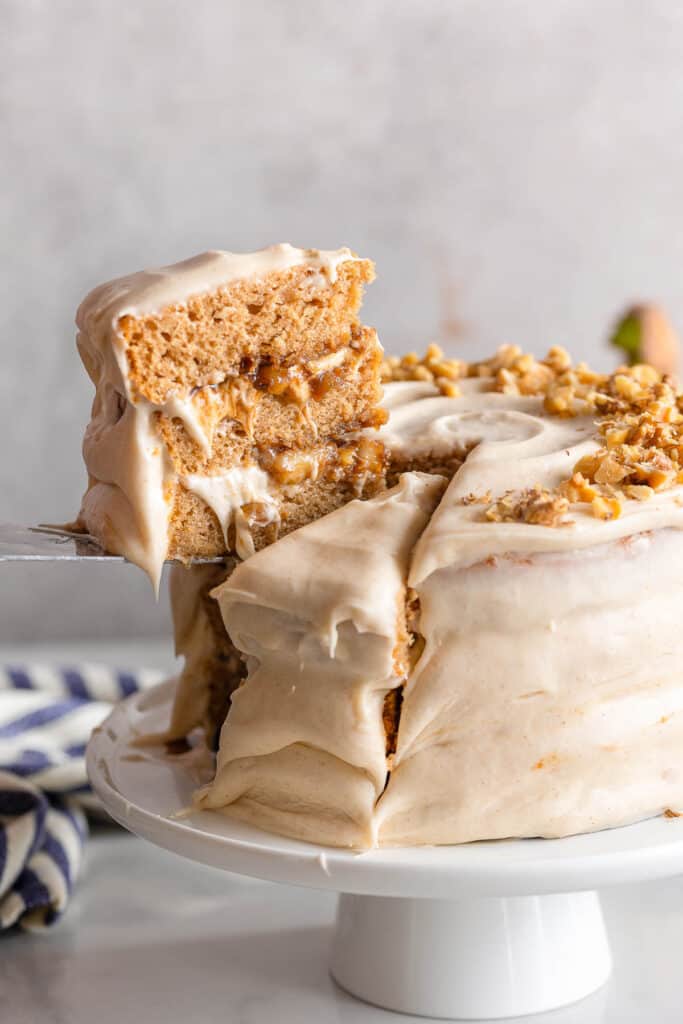 a Gluten Free Banana Cake & Cream Cheese Frosting slice held up over the cake