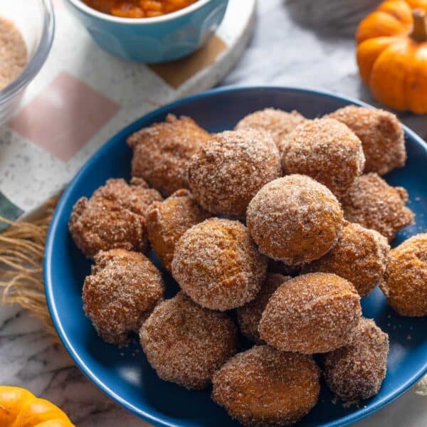 a plate full of Gluten Free Pumpkin Fritters coated in a cinnamon-sugar mixture with little pumpkins and pumpkin puree on the side