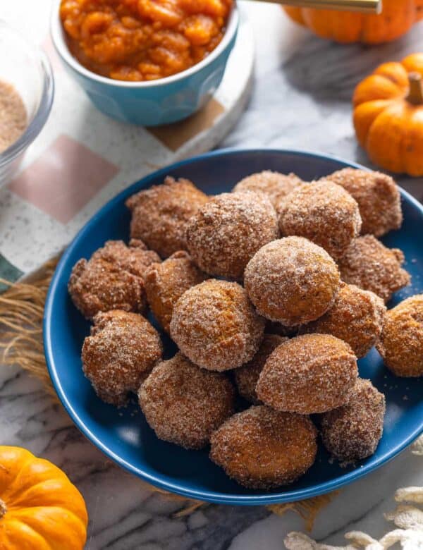 a plate full of Gluten Free Pumpkin Fritters coated in a cinnamon-sugar mixture with little pumpkins and pumpkin puree on the side