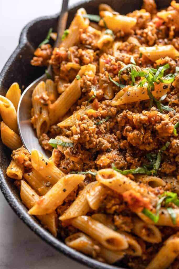 Pork Ragu with Penne topped with fresh sliced basil in a pan