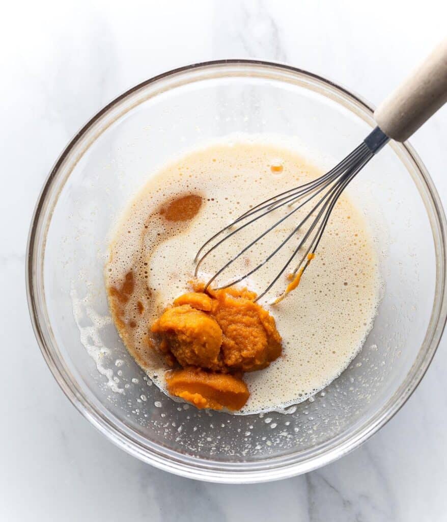 pumpkin puree and vanilla extract add to a bowl of whisked eggs and sugar