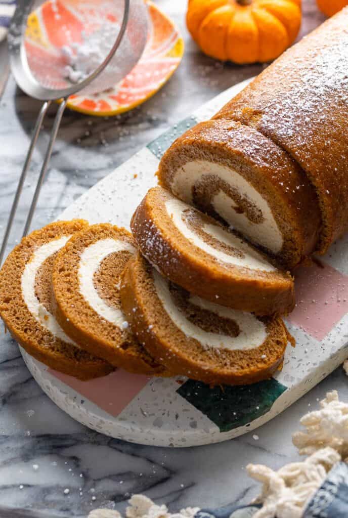 a loaf of Gluten Free Pumpkin Roll & Whipped Cream Cheese Frosting with thick slices cut into it