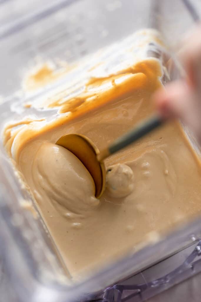 a spoon stirring creamy homemade cashew butter in a blender