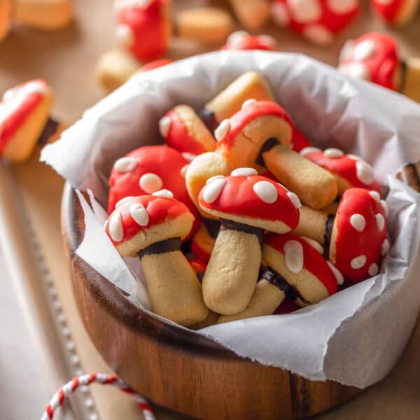 mushroom shaped sugar cookies decorated to look like red and white toadstool mushrooms in a bowl on a baking sheet