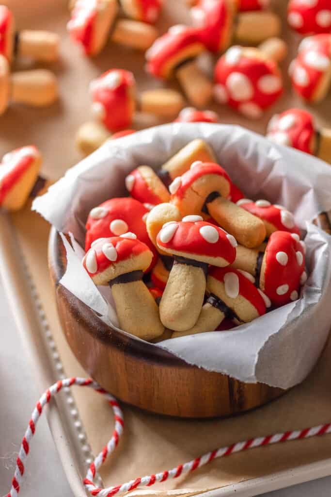 mushroom shaped sugar cookies decorated to look like red and white toadstool mushrooms in a bowl on a baking sheet