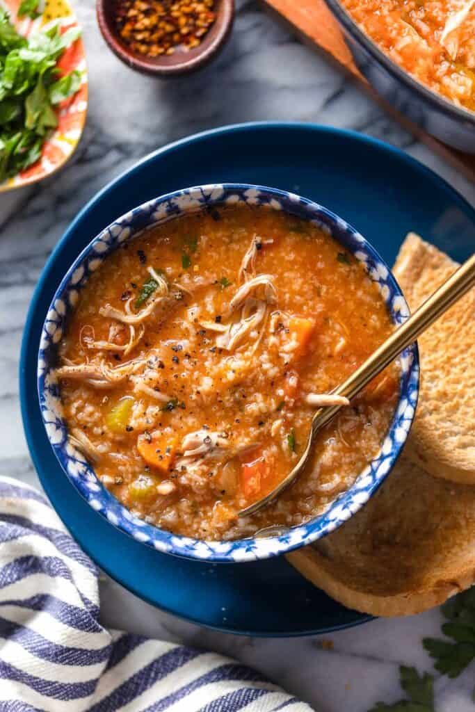 a bowl of Italian Tomato Chicken & Rice Soup with cracked pepper on top on a serving plate with toasted bread 