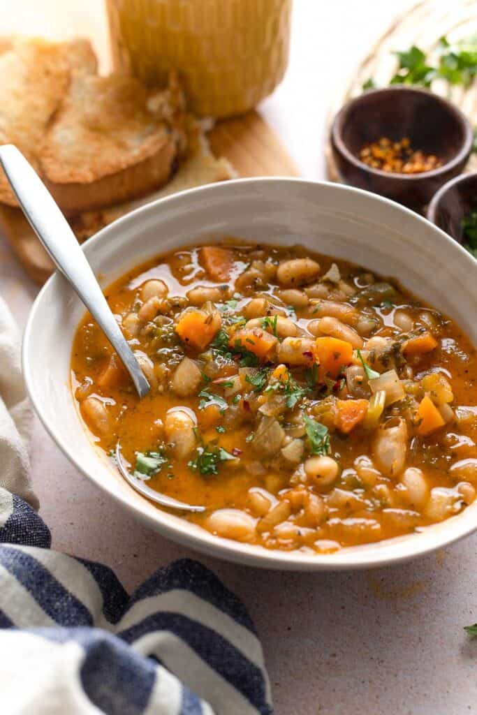 a bowl of fasolada soup topped with fresh parsley and chili flakes