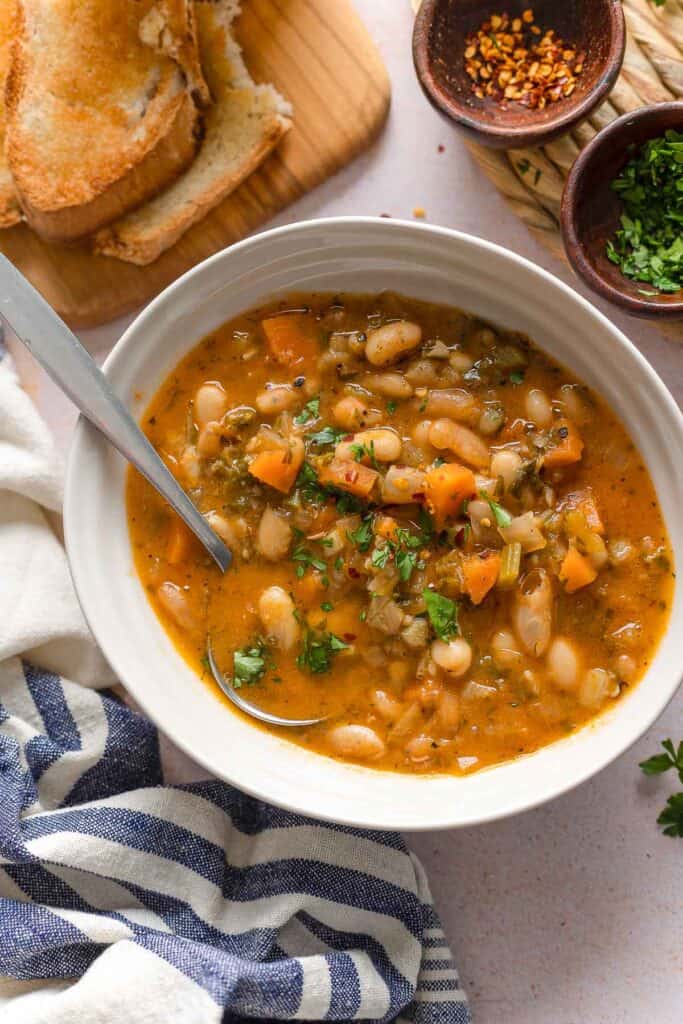 greek bean soup (also known as fasolada) in a bowl with chopped parsley and chili flakes  and a side of bread