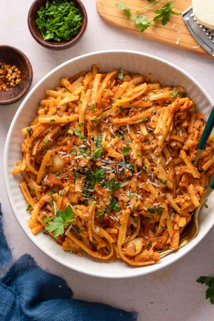 Linguini pasta mixed into a fish ragu sauce in a serving bowl topped with chopped parsley and parmesan