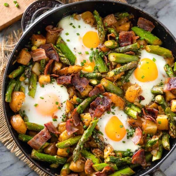 a cast iron skillet full of a Asparagus Potato Hash with Bacon & Eggs topped with fresh chopped chives