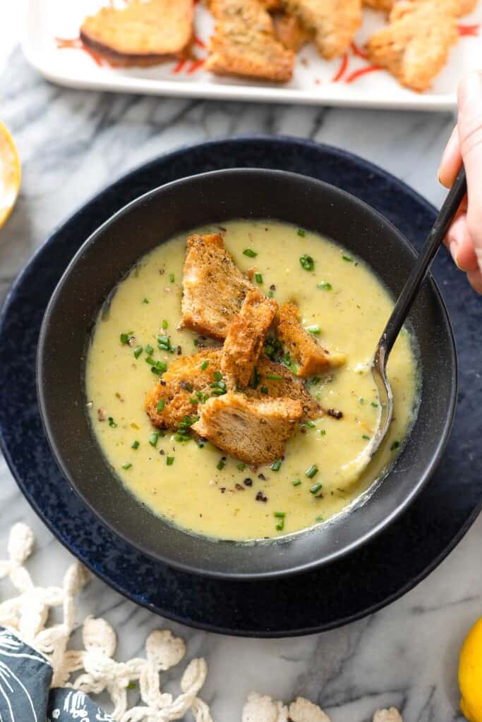 Asparagus Potato Soup in a bowl with a spoon topped with fresh chives and croutons