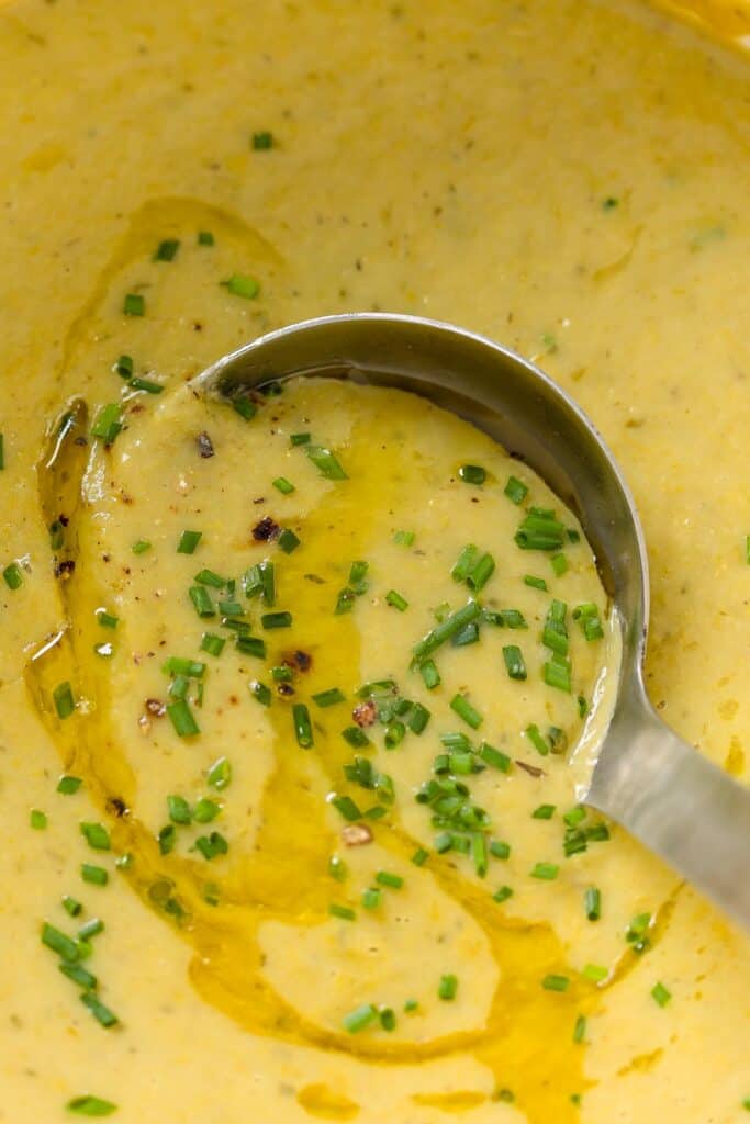 a ladle picking up Asparagus Potato Soup with fresh chopped chives and olive oil drizzled over the top