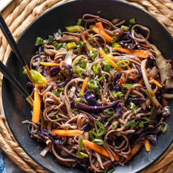 Carrot and Cabbage Noodle Stir Fry in a serving bowl with serving forks - topped with green onions and sesame seeds