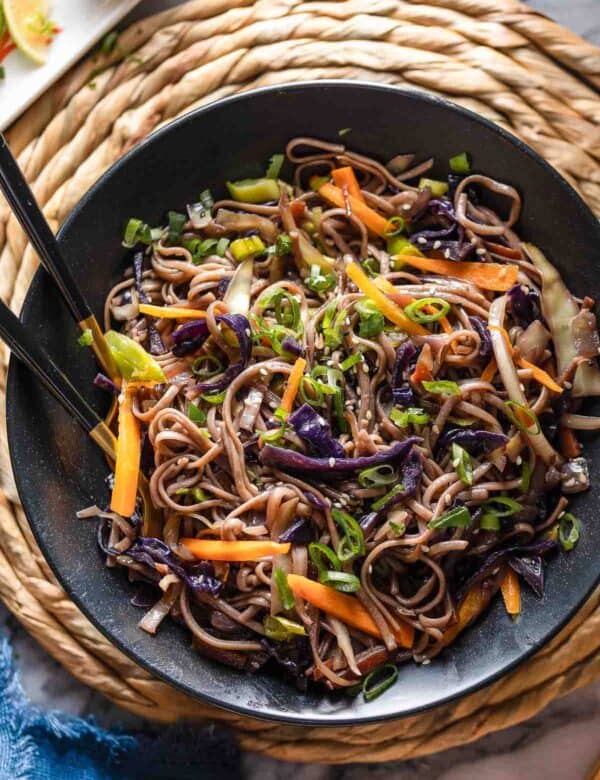 Carrot and Cabbage Noodle Stir Fry in a serving bowl with serving forks - topped with green onions and sesame seeds