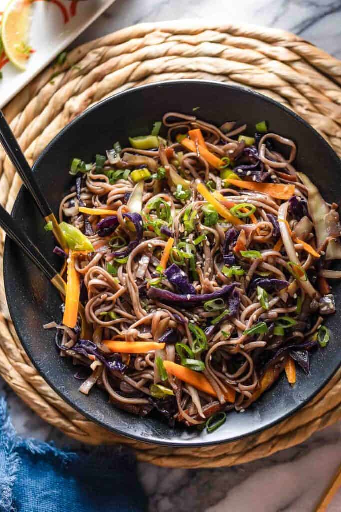 Carrot and Cabbage Noodle Stir Fry in a serving bowl with serving forks - topped with green onions and sesame seeds