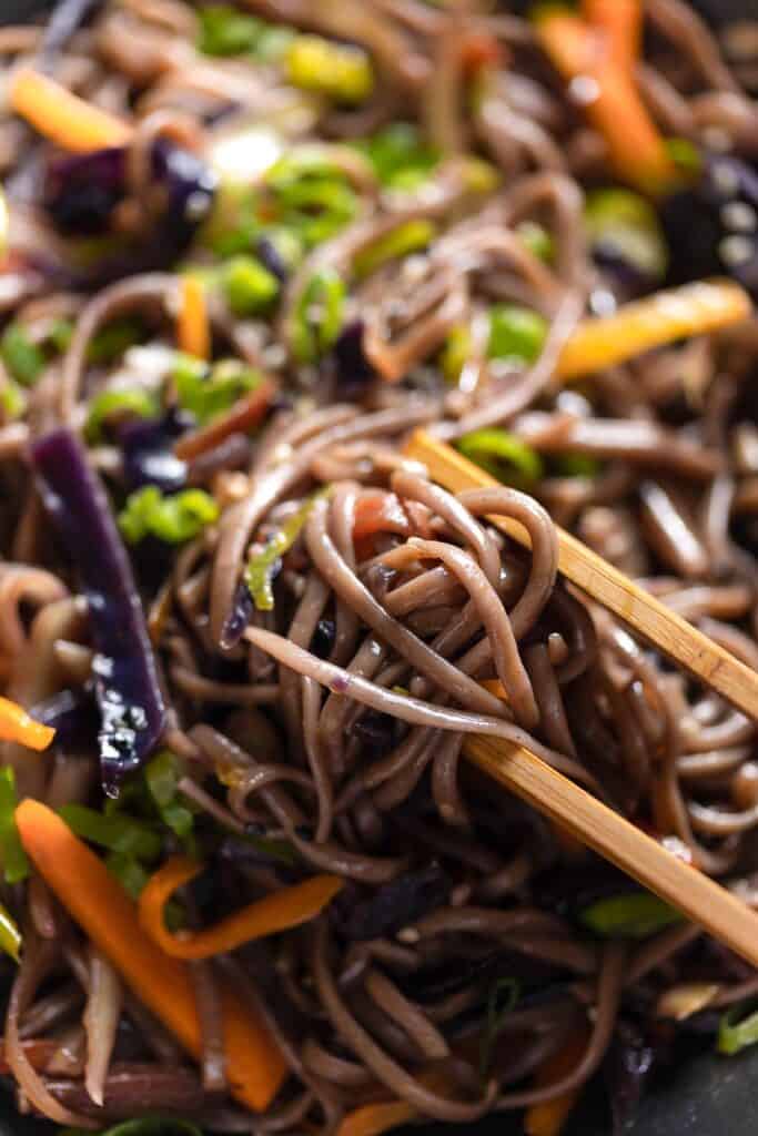 a pair of tongs holding up a serving of Carrot and Cabbage Noodle Stir Fry 