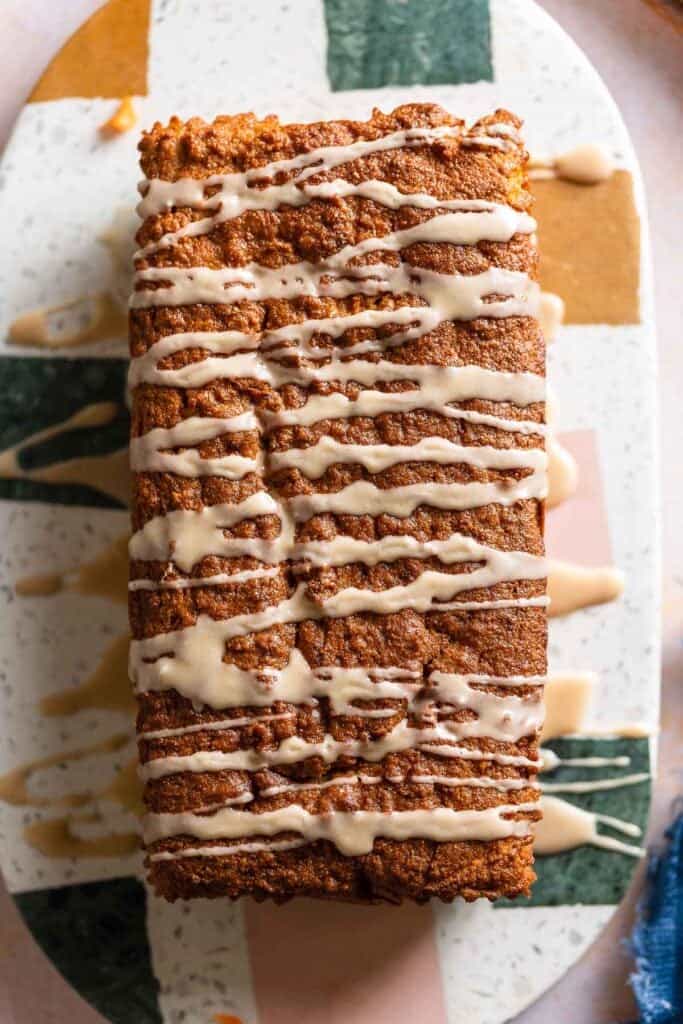 an uncut paleo coconut flour carrot cake on a serving platter with an icing drizzled over the top