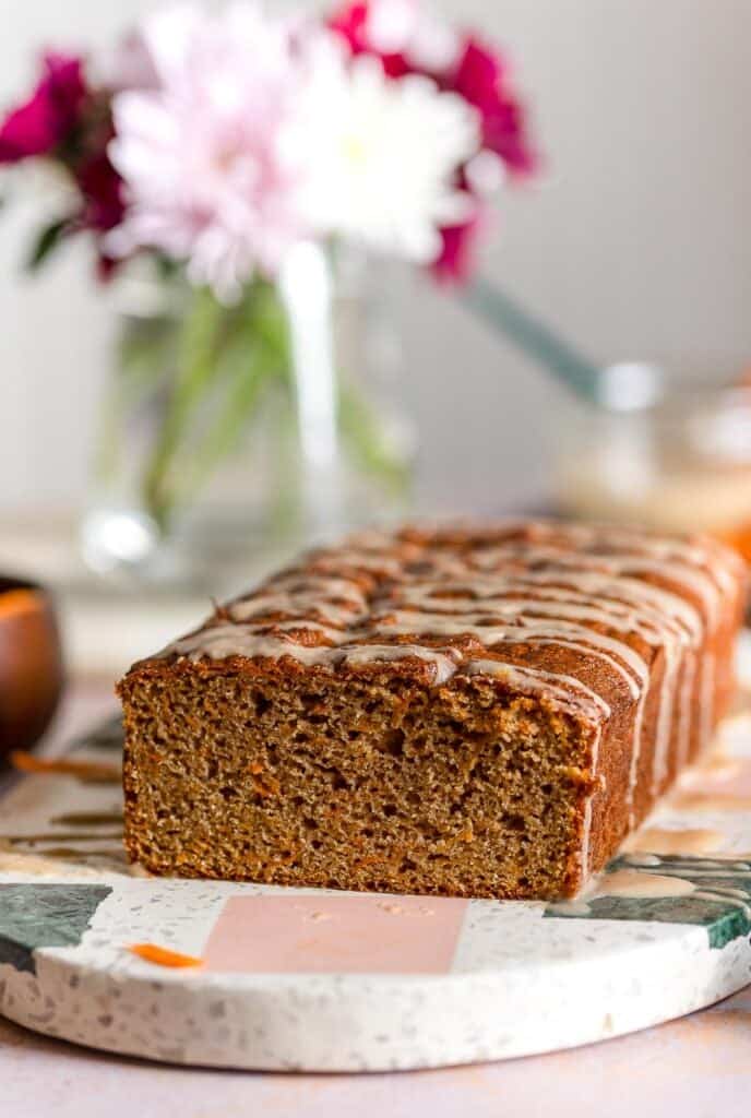 paleo carrot cake loaf with a slice cut off displayed on a serving platter