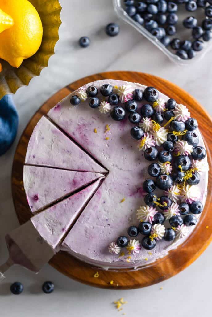 A Gluten Free Lemon Cake with covered in a blueberry mascarpone frosting and topped with fresh blueberries, lemon zest and little frostings stars piped with a 1C piping tip 