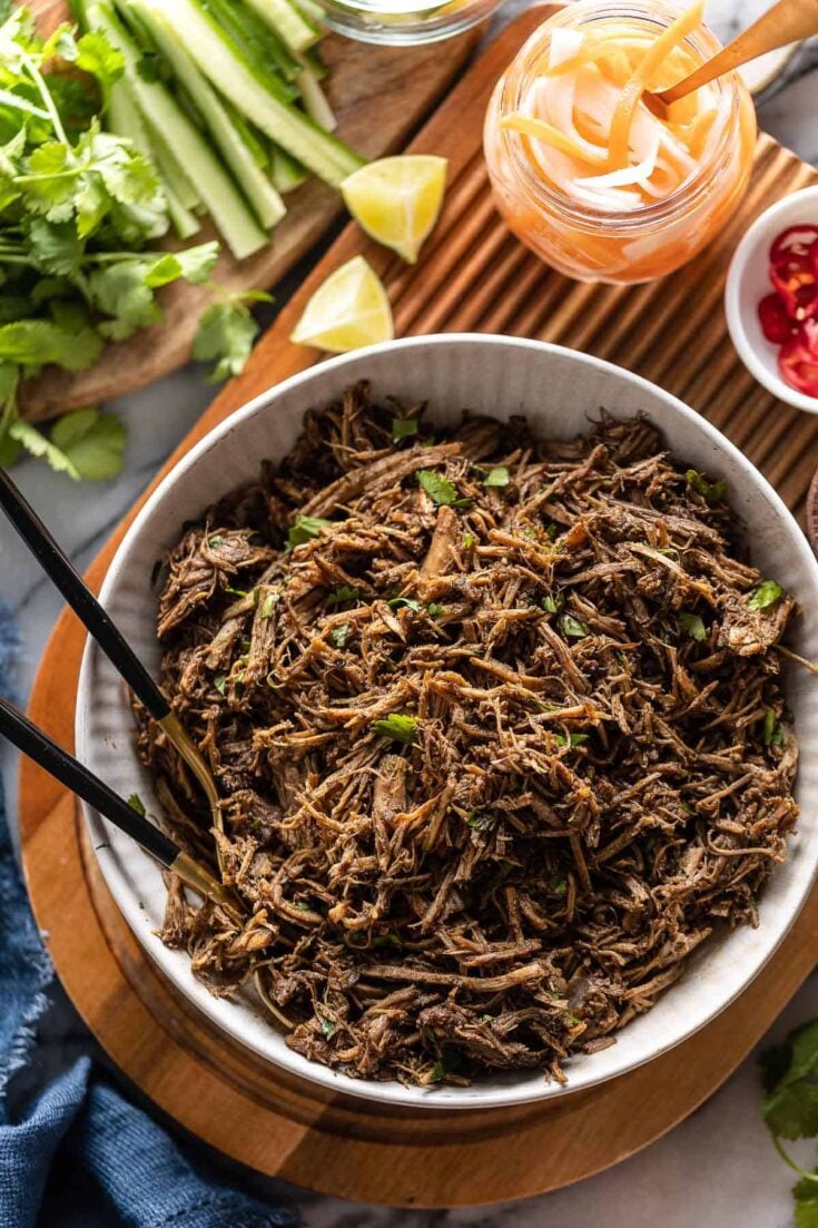 Vietnamese Five Spice Pulled Pork in a serving bowl with fresh cilantro mixed in an fresh, chopped and sliced veggies on the sides