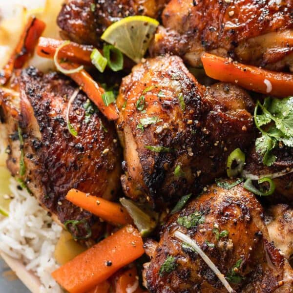 five spice chicken thighs over roasted carrot slices and cabbage wedges over a plate of white rice and topped with fresh cilantro and spring onions