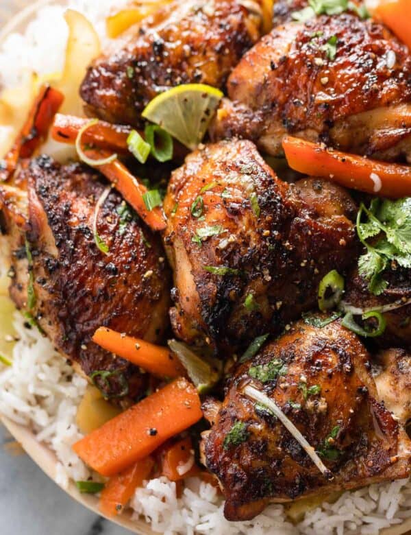 five spice chicken thighs over roasted carrot slices and cabbage wedges over a plate of white rice and topped with fresh cilantro and spring onions