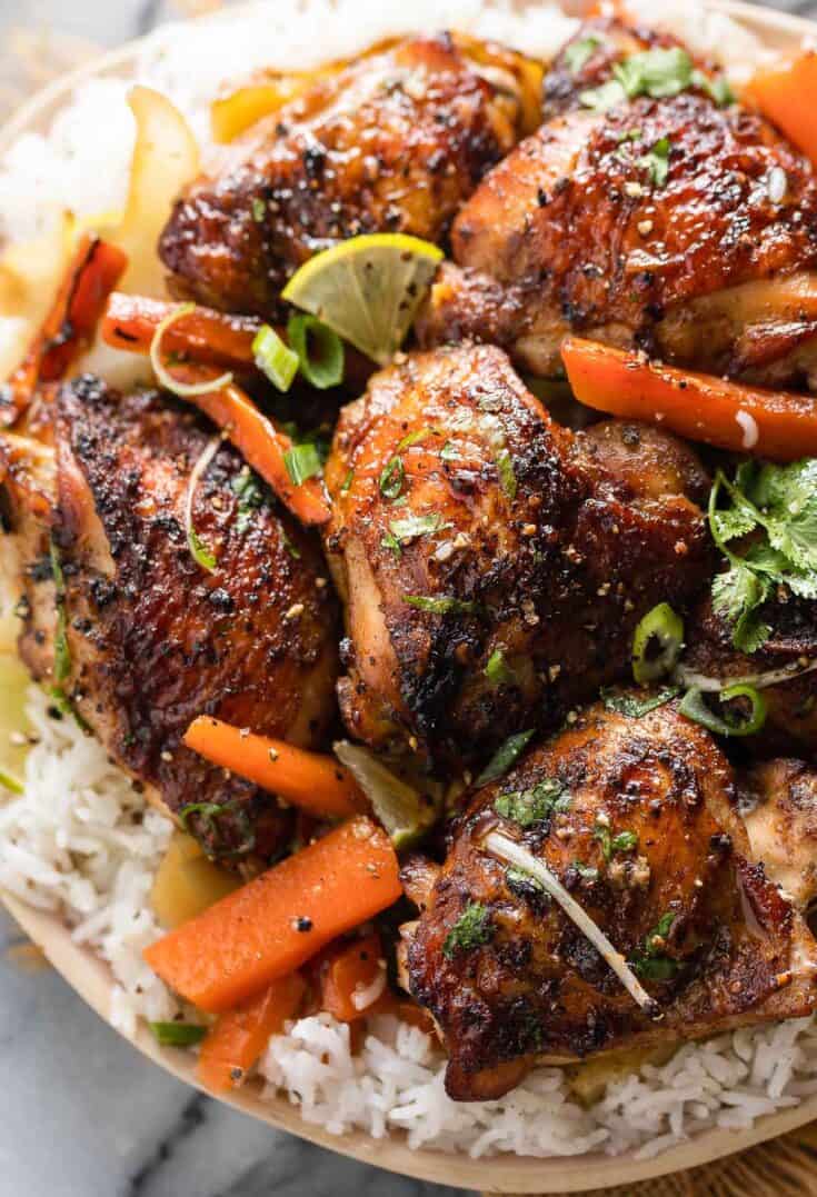 five spice chicken thighs over roasted carrot slices and cabbage wedges over a plate of white rice and topped with fresh cilantro and spring onions