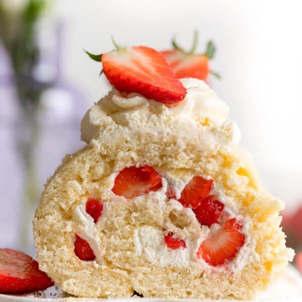 gluten free swiss roll cake on a platter topped with fresh strawberries and cream and a slice cut out