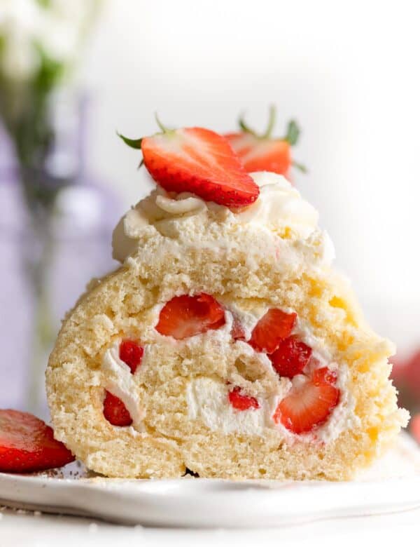 gluten free swiss roll cake on a platter topped with fresh strawberries and cream and a slice cut out
