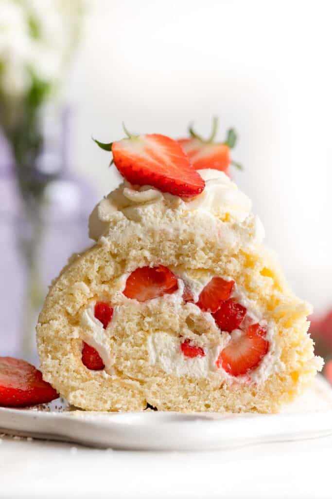 gluten free swiss roll cake on a platter topped with fresh strawberries and cream and a slice cut out