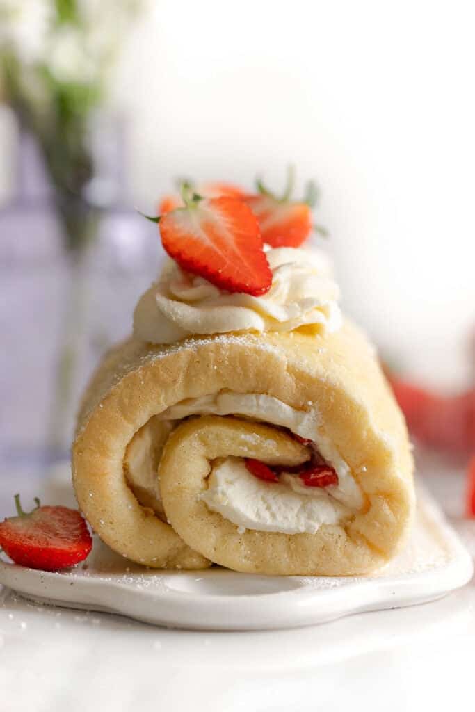 gluten free swiss roll cake on a platter topped with fresh strawberries and cream