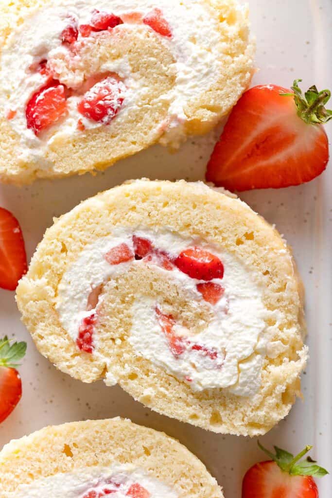 gluten free swiss roll cake slices with strawberries and cream filling on a platter with fresh strawberries