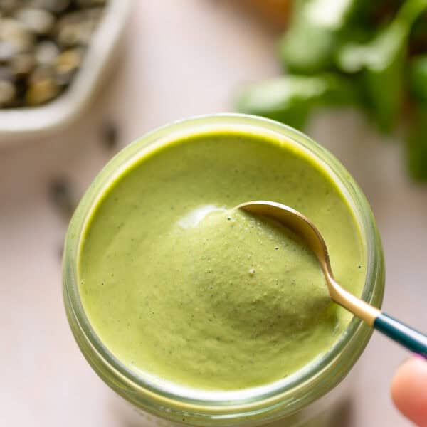 a spoon stirring Cilantro Pepita Dressing in a jar